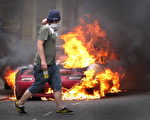 一名蒙面的年輕人從一輛正在燃燒的汽車前經過。(Peter Macdiarmid/Getty Images)