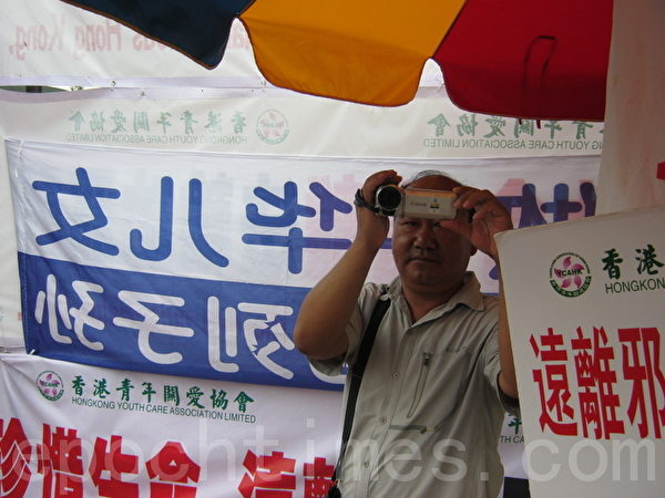 在曾慶紅、梁振英授意下,青關會雇傭配備專業攝影器材來滋擾香港法輪功真相點的幫兇。(大紀元圖片) 在曾慶紅、梁振英授意下,青關會雇傭配備專業攝影器材來滋擾香港法輪功真相點的幫兇。(大紀元圖片)
