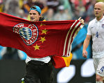 截至世界盃1/4決賽前，拜仁慕尼黑已經獲得足聯一百多萬歐元世界盃球員出場費，領先歐洲各大豪門俱樂部。圖為一位德國球迷展示了支持中場球員邁克爾·布拉德利的拜仁慕尼黑足球會圖案毛巾。（NELSON ALMEIDA／AFP）