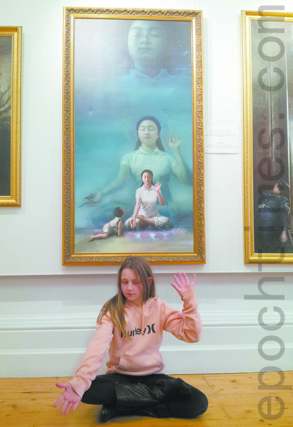 澳洲女孩何莉坐在《纯净入仙境》画作前,模仿著画中女修炼者的姿势打手印,家人很高兴,一家人表示要去炼功点学功。(摄影:李梅/大纪元) 澳洲女孩何莉坐在《纯净入仙境》画作前,模仿著画中女修炼者的姿势打手印,家人很高兴,一家人表示要去炼功点学功。(摄影:李梅/大纪元)