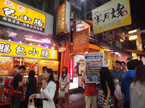 在台灣台中逢甲夜市知名攤販前，排隊的人龍不時望向法輪功真相展板。（黃玉燕／大紀元）