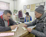 12月31日，谭先生（右）手中拿着50元到纽约中华公所捐款。（摄影：蔡溶/大纪元）