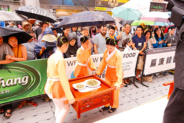 6月27日，第七届新唐人全世界中国菜厨技大赛决赛在纽约时代广场举行。当天下午下起了雨，观众打伞观看比赛，不愿离去。（戴兵/大纪元）