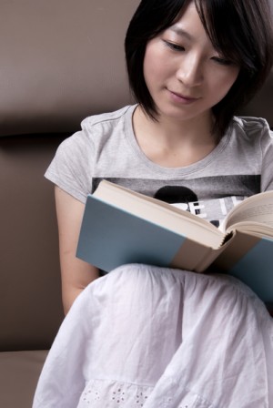 Portrait of a young woman sitting on sofa reading book(shutterstock) Portrait of a young woman sitting on sofa reading book(shutterstock)