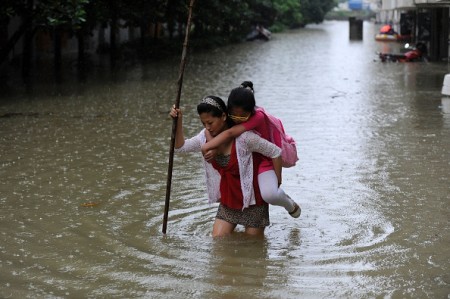This picture taken on July 5, 2016 shows a woman carrying her daughter through a flooded area in Zongyang county, in east China's Anhui province. Heavy rain around China's Yangtze river basin has left 128 people dead and scores missing, media said on July 5, with more damage feared from a typhoon expected to land this week. / AFP / STR / China OUT (Photo credit should read STR/AFP/Getty Images)