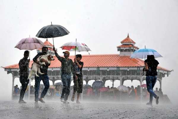 中共的御用“智库”对印度的崛起进行了错误的解读，误导了中国人民。图为今年6月印度梅雨期间行人带着狗路过一个庇护所。（Getty Images）