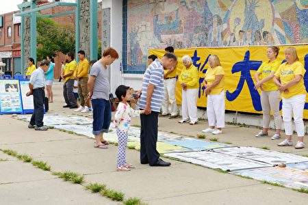 2016年7月30日,來自中部十個州的法輪功學員匯集在芝加哥中國城舉行盛大的遊行。圖為華人民眾閱讀法輪功煉功點的真相展板。(陳傑傑/大紀元)