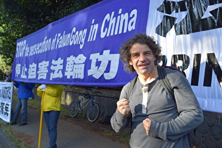 图说:2016年9月26日,温哥华市中心的中领馆前,路人Shlomo Mcpeake先生在法轮功学员的横幅前留影表示声援。(唐风/大纪元)