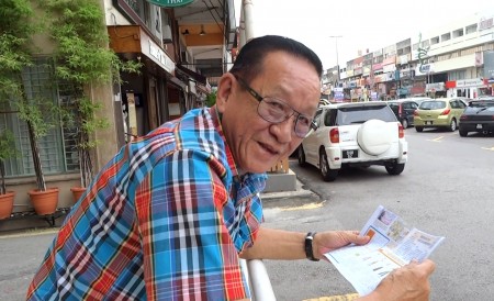 當地老居民周先生,在法輪功遊行隊伍走過後,仍然逗留在同樣地方細心的閱讀法輪功簡介。(明慧網)