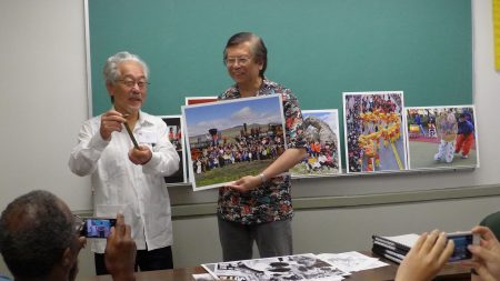 紐約華裔攝影師李揚國與多倫多客家會議發起人羅金生(Keith Lowe,左)在會上,李揚國介紹他與一些華人,在橫跨鐵路建成145周年之際,號召了200名華人和其他亞裔,在複製的火車機車前面合影,彌補當年鐵路完工慶祝活動照片看不到華工身影的缺憾,他們還步行到數英里外的中國拱門。