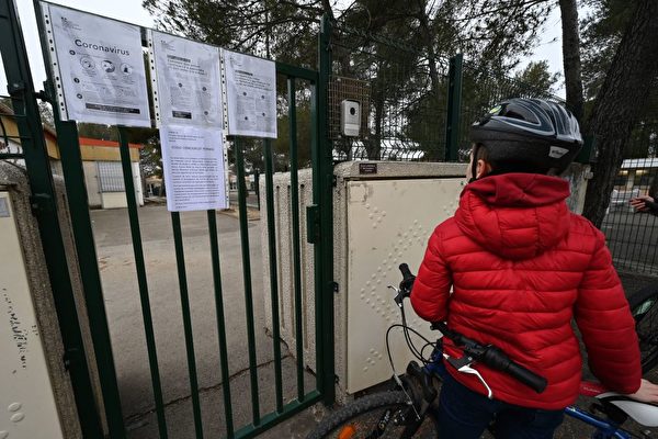 2020年3月12日，一個法國男孩在其關閉的學校的大門前閱讀關於中共肺炎的信息。 (Photo by PASCAL GUYOT/AFP via Getty Images)