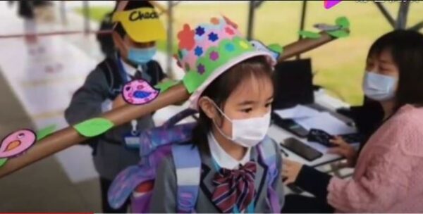 杭州錢塘新區養正小學要求家長給孩子製作「一米帽」用於保持一米的距離。（視頻截圖）