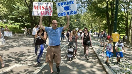 埃里克（Erich）在遊行隊伍中舉著兩個反對要求兒童戴口罩的標語。