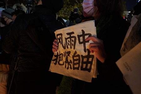 2022年11月29日，民眾在紐約中國留學生於中領館對街舉辦的集會中，手持寫有「風雨中抱緊自由」的展板。
