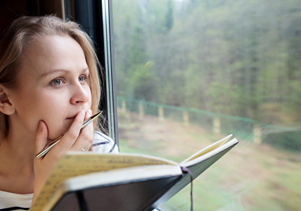 Young Woman On A Train Writing Notes In A Diary