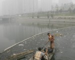 2007 年7月26 日北京运河漂浮着大量垃圾，工作人员驾着小船试图清理。（TEH ENG KOON/AFP/Getty Images)