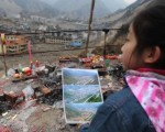 北川三道拐，一个孩子手拿北川地震前照片对照眼前的惨状。