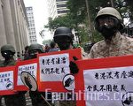 5位抗議人士身穿整齊的全副軍裝，頭戴鋼盔，面帶防毒面具的「解放軍」，手持以拿槍軍人為裝飾圖的抗議標語牌。（攝影：梁路思／大紀元）