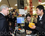 2月17日，哈珀总理（左）到多伦多金牛城超市看望陈旺（右），并购买了一包金桔与一瓶枫树糖浆。陈旺妻子（中）帮哈珀总理把糖浆用纸包好。（摄影：周月谛/大纪元）
