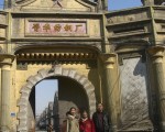 老晉華紡織廠的大門，門後可見上世紀二十年代的廠房和庫房。前面老人是作者的妹妹 張文采，她左右各一人，是她的孩子及孫子。（作者提供之近日相片）
