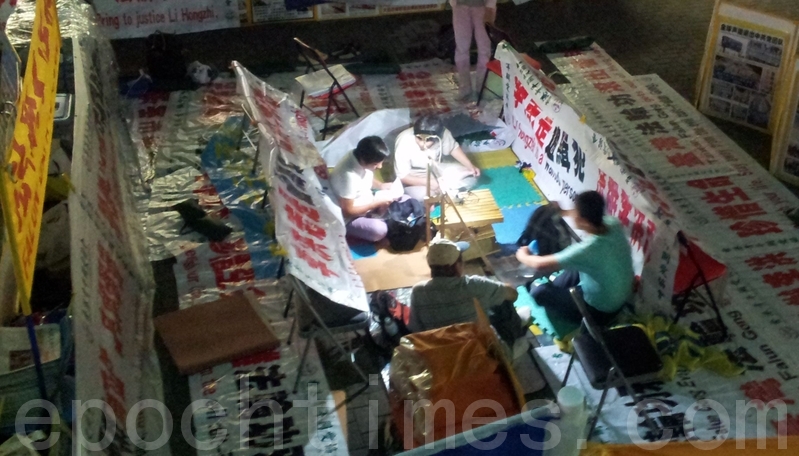 在九龍紅磡火車站外,十年來法輪功學員設了退黨真相點給往來香港的大陸人退黨及講法輪功在大陸遭迫害的真相,晚上都會離開,第二天早上再來。但現在他們被協會的橫幅團團包圍住,因橫幅上寫有法輪功創始人的名字,他們不想踐踏,故守在原地。他們曾多次與在場警員交涉,要警員拿開協會地上的橫幅,讓一條路給他們出去,警員都不作為。(大紀元)