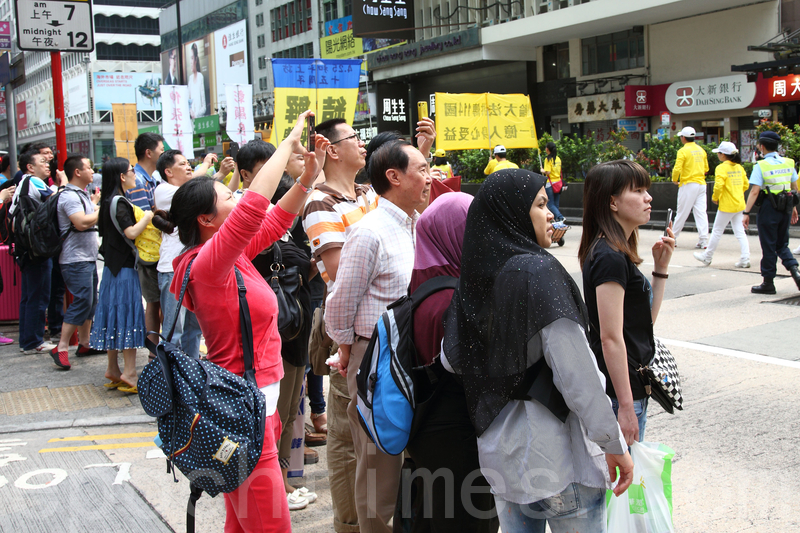 香港法轮功学员4月20日举行声势浩大的游行,纪念“四.二五”和平大上访15周年,大约八百人游行队伍沿着九龙的闹市区,途经多个大陆游客购物热点,吸引两旁的大批游客观看,许多人拿着手机和相机争相拍摄。(潘在殊/大纪元)