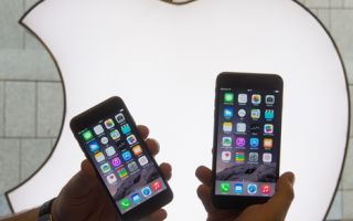 受新款大屏幕iPhone销售推动，苹果第四季度利润大增13%。图为一名德国的果迷在苹果商标前手拿2支新款大屏幕iPhone手机。（PETER KNEFFEL/AFP/Getty Images）