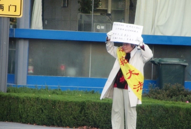 山东省龙口市法轮功学员吴曼萍为营救遭当局绑架的丈夫尹向阳,在龙口市委市政府举牌抗议。(明慧网)