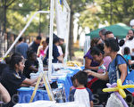 华人、西裔人士在当地赞助商的摊位前领取食物和介绍资料、礼物。大人、孩子嬉笑欢乐。（杜国辉/大纪元）