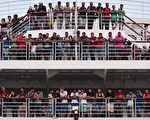 2015年8月21日，希腊政府特别派出接运叙利亚难民的渡轮在比雷埃夫斯抵达口岸时，难民们站在甲板上。当局另外也派出一艘大型渡轮抵科斯岛。希腊当局的计划是让2,500名叙利亚难民上船暂住，同时进行登记。(LOUISA GOULIAMAKI/AFP/Getty Images)