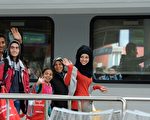 2015年9月6日，德國南部慕尼黑，來自匈牙利的難民通過奧地利搭乘火車到達德國，受到當地數千志願者的歡迎和迎接。圖為經過千幸萬苦最終到達慕尼黑的難民們露出笑容，高興地揮手。(CHRISTOF STACHE/AFP/Getty Images)