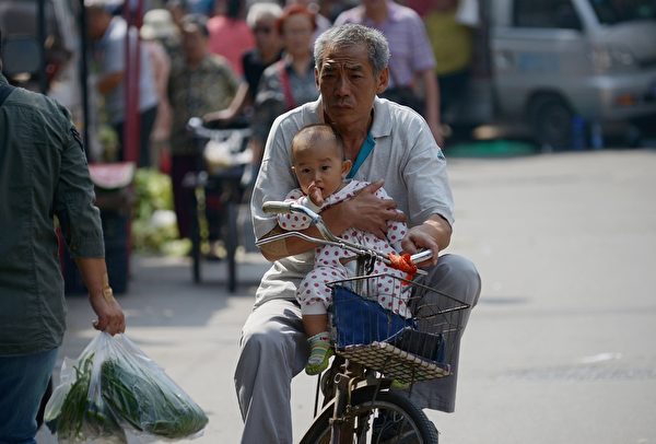 2015年9月8日，一个老人抱着一个孩子，骑车走在北京的街头上。单凭老龄化这一点，所谓的“计生”好处就不可能实现。（WANG ZHAO/AFP/Getty Images）