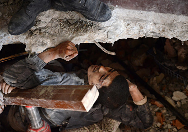 2015年4月26日，尼泊尔加德满都，救援人员救助一名被埋在废墟里的幸存者，他朋友的遗体就躺在他身边。该国8.1级强震导致的遇难人数已经上升至2200人。救援人员26日徒手挖掘残垣断瓦，盼救出生还者。(PRAKASH MATHEMA/AFP)