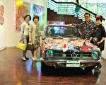 艺术家林庆芳（右后）展出的古董车装置艺术，全车包覆鲜艳的尪仔标。（赖月贵／大纪元）