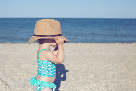Cute toddler girl in big hat on the beach