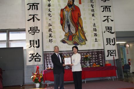 徐儷文(右)代表中華民國僑務委員會委員長吳新興,向剛卸任的老校長黃炯常(左)頒發「功在僑校」的賀匾。