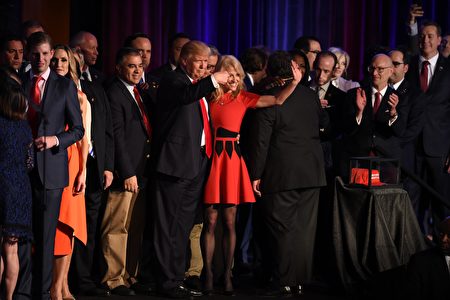 在勝選演講後合影時，川普以左手臂環抱康威的腰，在她向群眾揮手致意時，右手食指驕傲又感激地指著她。(TIMOTHY A. CLARY/AFP/Getty Images)