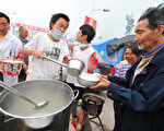 2008 年5月，四川汶川地震，志愿者为灾民分发米粥。(FREDERIC J. BROWN/AFP/Getty Images)