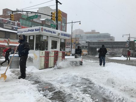 9日早上人们在清扫法拉盛图书馆前人行道的积雪，法拉盛中心区空空荡荡。