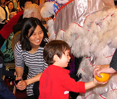 波士顿市议长吴弭（中）的儿子Blaise（右）拿到舞狮中派送的橘子，格外高兴。(贝拉/大纪元)
