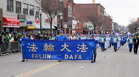 波士頓聖派翠克節遊行隊伍中，身著藍白相間中國傳統服裝的160名樂團成員，手舉「法輪大法」橫幅，方陣整齊，氣勢雄壯。（貝拉/大紀元）