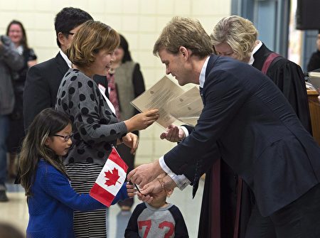 图说：2014年10月，前任移民部长Chris Alexander在入籍典礼上给一家中国移民发放加拿大国旗。（加通社）