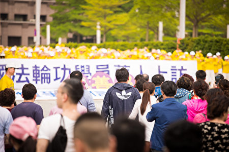 台灣法輪大法學會4月16日在台北市政府前市民廣場舉行「紀念4.25中國法輪功學員萬人和平上訪18周年」活動。經過的陸客駐足觀看，並拿起手機拍照。（陳柏州／大紀元）