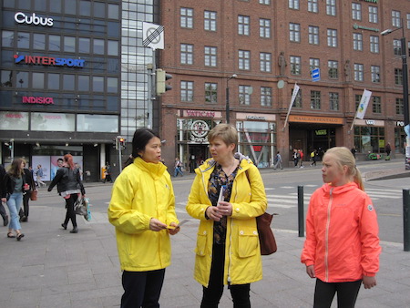 27日，法輪功學員（左）在赫爾辛基市中心向民眾講述迫害真相。（李樂／大紀元）