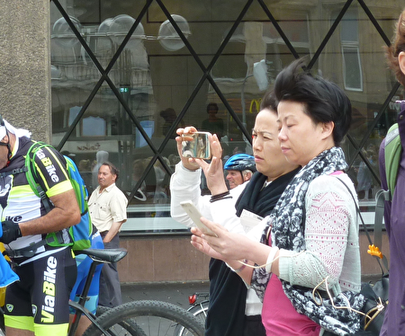 兩位中國大陸游客在科隆大教堂前拍攝法輪功學員的方陣，一位已經拍完，正在檢查拍攝效果，一位正在拍攝。（文婧／大紀元）