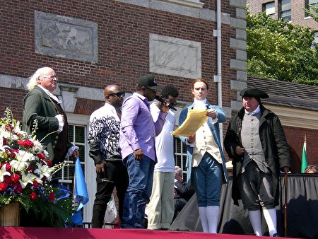 費城知名的R＆B聲樂組--「Boyz II Men」的三位主要成員在慶祝美國誕生241周年的儀式上，誦讀「獨立宣言」的一部分。美國國家公園管理局費城分支的工作人員裝扮成本 . 富蘭克林等開國元勛與他們同台。（司瑞/大紀元）