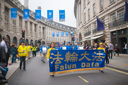天國樂團和法輪功學員組成的遊行隊伍穿過倫敦唐人街，街邊有行人駐足觀看。（Laphare／大紀元）