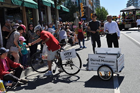 圖：北溫市長Darrell Mussatto在遊行的間隙時間裏，向路邊觀眾分發糖果並互祝快樂。（唐風/大紀元）