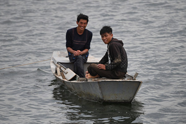 两名朝鲜男子在鸭绿江上以中国游客微笑。（GREG BAKER / AFP / Getty Images）