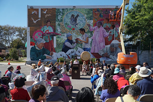 10月4日，宾州亚裔老人服务中心PASSi创办人及总裁崔英佳女士（Im Ja Choi） 在壁画揭幕剪彩前演讲。右上方艺术家Ann Northrup正在装上最后一片壁画。（肖捷/大纪元）